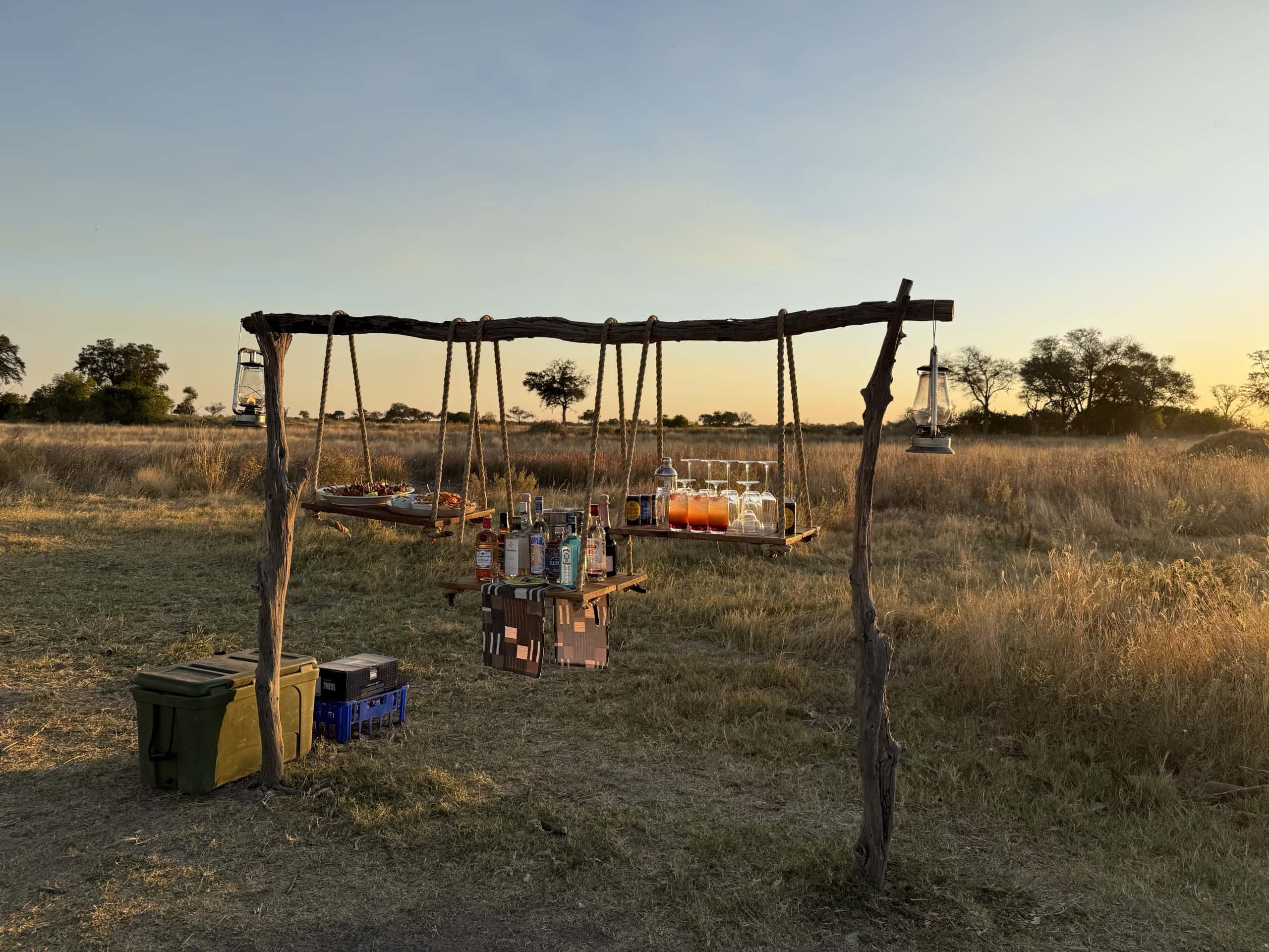 A bar hung in the grass at golden hour: lanterns, glasses and open savannah