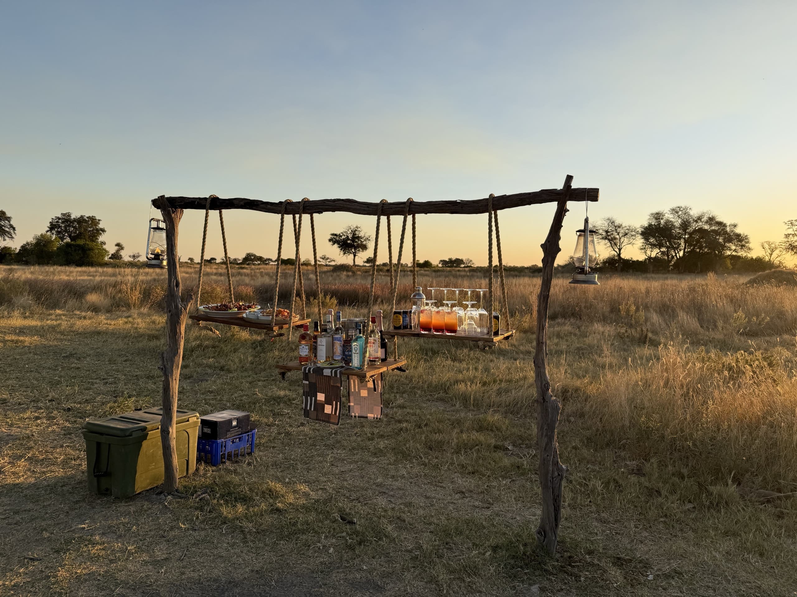 A bar hung in the grass at golden hour: lanterns, glasses and open savannah